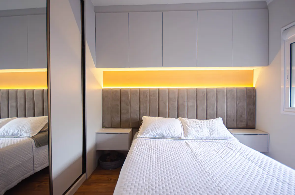 Quarto planejado com cabeceira estofada, painel iluminado e roupeiro com portas de espelho